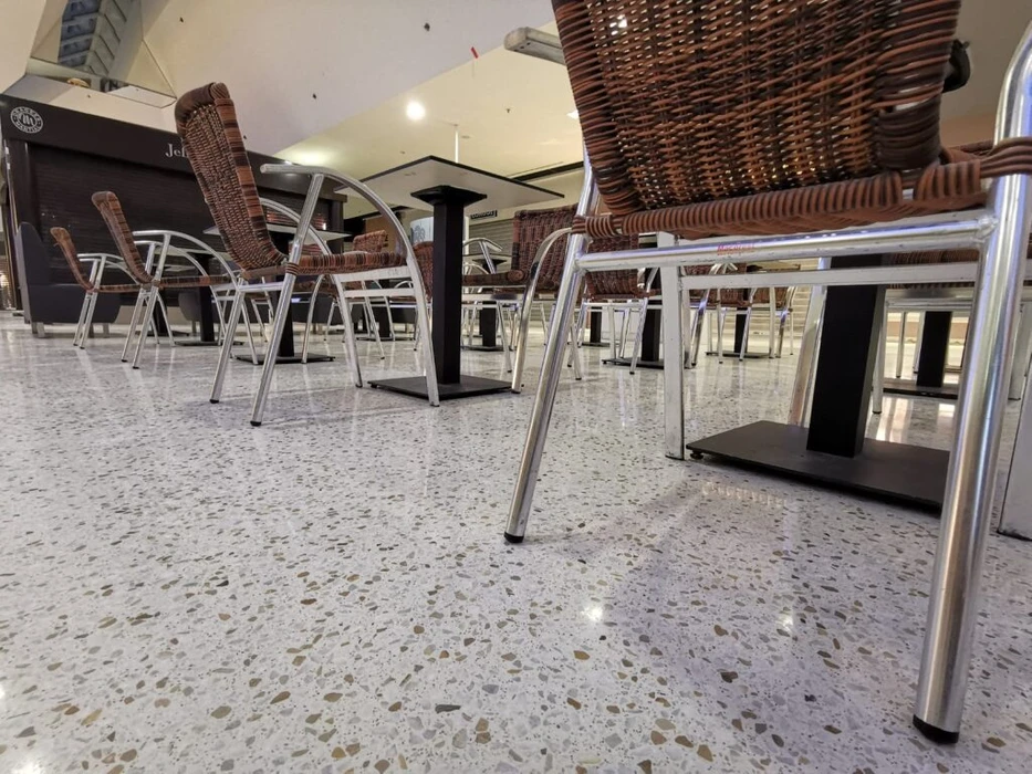 Vaste espace commercial vide de type showroom, sol en béton poli brillant, plafond à dalles acoustiques noires avec spots LED encastrés et structure métallique apparente