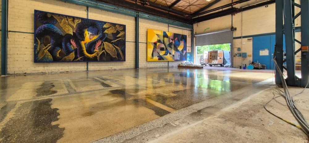 Espace commercial vide en cours de rénovation, sol en béton ciré poli réfléchissant, murs blancs avec zone peinte en anthracite et teal