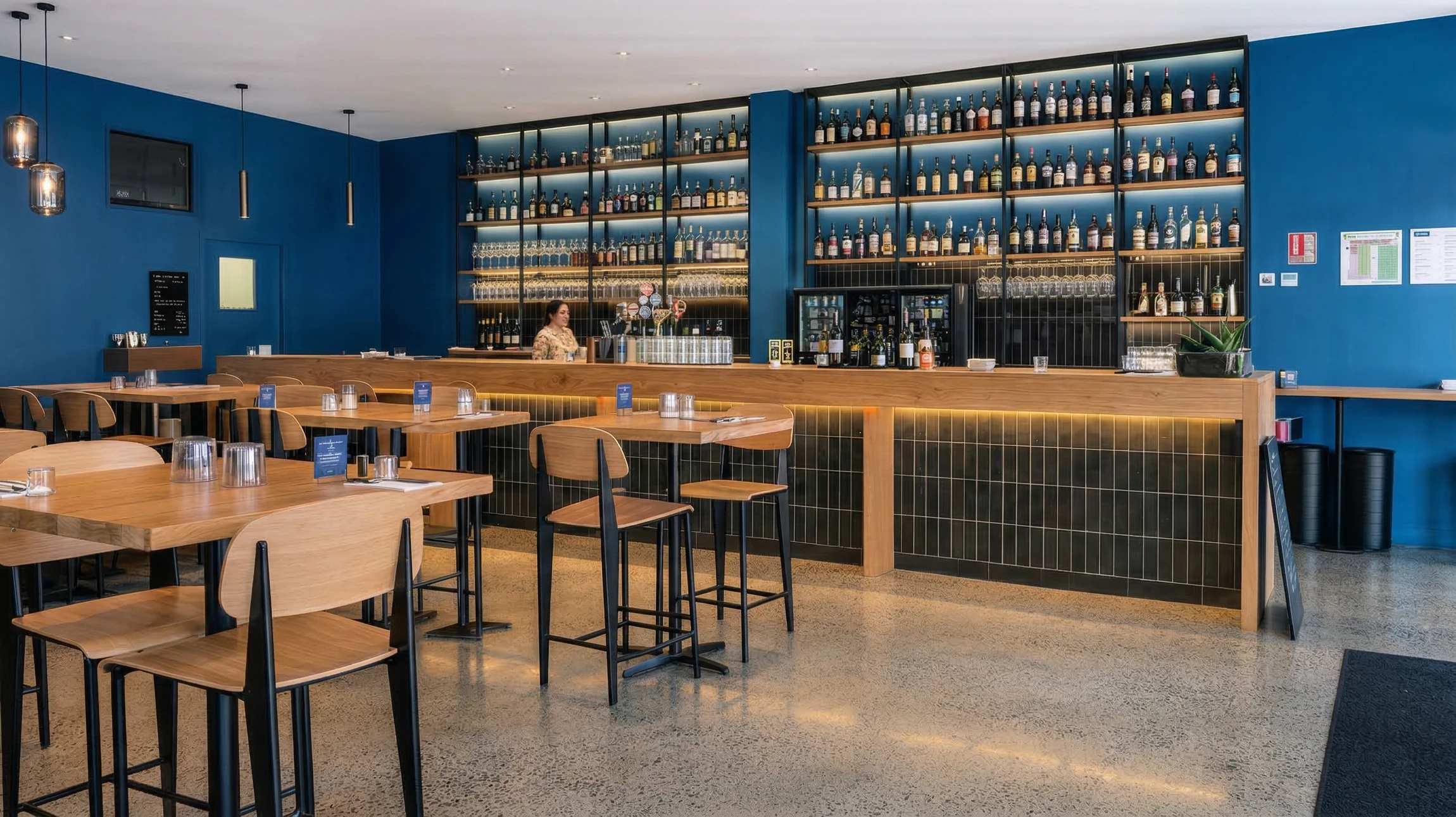 Ouvrier professionnel en tenue de sécurité (casque, gilet, chaussures de protection) utilisant une monobrosse de polissage industrielle ou une ponceuse spécialisée sur une vaste surface de dalle béton grise dans un hall ou atelier. La surface béton visible montre des zones avec un aspect mat à poli, illustrant le processus de transformation. Lumière naturelle ou professionnelle mettant en valeur le contraste entre les zones travaillées et non travaillées du béton. Mise au point sur l'outil et la surface de travail, cadrage horizontal type "hero".