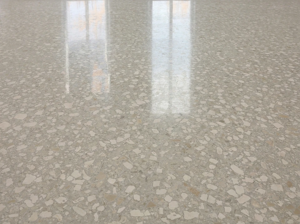 Ouvrier en vêtement blanc utilisant une ponceuse à béton électrique sur sol en béton brut dans un espace intérieur